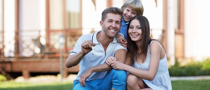 Happy family of three smiling outdoors in front of house with green lawn